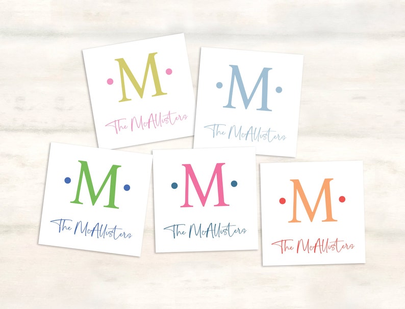 K&ouml;nnte beinhalten: F&uuml;nf wei&szlig;e quadratische Karten mit dem Buchstaben "M" in verschiedenen Farben. Jede Karte tr&auml;gt den Text "The McAllisters" unter dem Buchstaben.