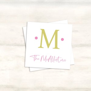 K&ouml;nnte beinhalten: Eine wei&szlig;e Karte mit einem goldenen Buchstaben "M", umgeben von zwei rosa Punkten. Der Text "The McAllisters" ist in rosa Kursivschrift unter dem Buchstaben geschrieben.