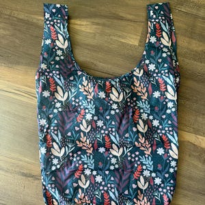 May include: A reusable shopping bag with a floral pattern in shades of pink, blue, and red on a dark blue background.