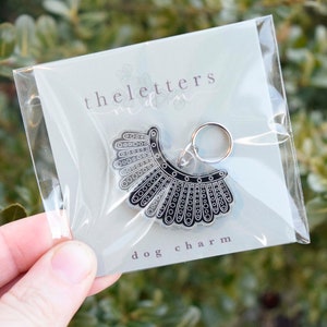 May include: A black and silver dog charm in the shape of a judge's collar. The charm is packaged in a clear plastic bag with a white card that reads "theletters" and "dog charm".