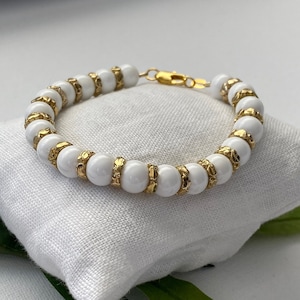 Armband aus 8 mm großen polierten weißen Perlmutt-Muschelperlen mit feinen vergoldeten Elementen.