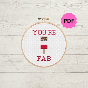 Könnte beinhalten: Ein weißer Kreuzstich-Stickrahmen mit dem Text "YOU'RE FAB" in rotem Garn. Ein rotes und weißes Eis am Stiel mit bunten Streuseln ist in der Mitte des Rahmens gestickt.