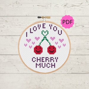 Puede incluir: Patrón de punto de cruz con dos cerezas rojas con caras sonrientes y un tallo verde en forma de corazón. El patrón incluye el texto "I love you cherry much" y corazones rosas.