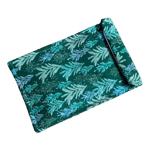 May include: A rectangular, rolled-up placemat with a dark green background and a repeating pattern of stylized, light blue and teal fern fronds. The placemat is made of fabric and has a white border.