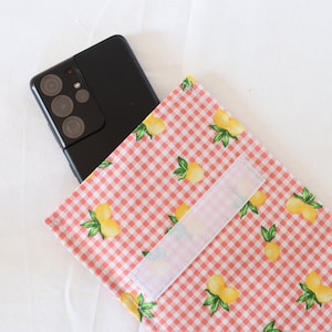 Op de afbeelding: Een roze en witte geruite telefoonhoes met een citroenprint en een witte klittenbandsluiting.