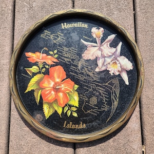 May include: Round black tray with a gold rim featuring a map of the Hawaiian Islands, hibiscus flowers, and orchids. The words "Hawaiian" and "Islands" are printed on the tray.