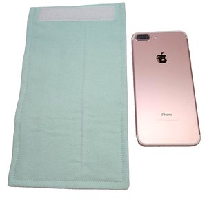 Op de afbeelding: Een lichtgroene stoffen tas met een witte klittenbandsluiting. De tas is ongeveer zo groot als een smartphone. De tas wordt getoond naast een roze gouden iPhone.