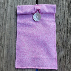 Op de afbeelding: Een roze stoffen tas met een witte knoopsluiting. De tas heeft een wit bloemenpatroon.