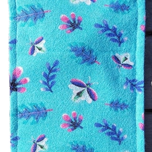 Op de afbeelding: Een turquoise stoffen brillenkoker met een patroon van gestileerde vlinders en bladeren in roze, wit en blauw. De rechthoekige koker heeft een gevouwen klepsluiting.