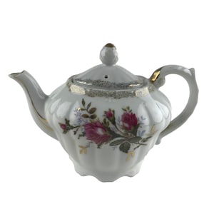 May include: White porcelain teapot with a gold trim and a floral design featuring pink roses. The teapot has a lid with a small knob on top.