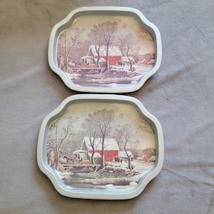 May include: Two vintage metal trays with a winter scene featuring a red barn, horses, and a bridge. The trays have a light blue scalloped edge and a detailed illustration of a snowy landscape.