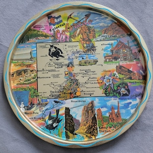 May include: A round, vintage Colorado souvenir tray with a gold rim and a turquoise wavy border. The tray features a map of Colorado with illustrations of landmarks, including Pikes Peak, the Royal Gorge, and the Garden of the Gods.