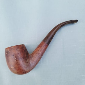 May include: A curved tobacco pipe crafted from light brown wood with a darker brown stem. The bowl features a natural wood grain pattern, and the shank is engraved with the text REAL BRIAR YEDA RADION, showing a smooth, polished finish.