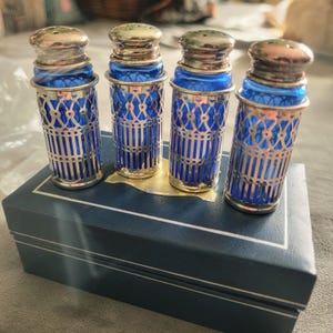 May include: A white ceramic mug with a black handle and the text "But First, Coffee" in a bold, black font. The mug is set against a blurred background, suggesting a cozy setting.