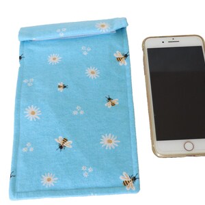 Op de afbeelding: Een lichtblauwe telefoonhoes met een wit madeliefje en bijenpatroon. De hoes is gemaakt van stof en heeft een flap die sluit met een klittenbandsluiting.