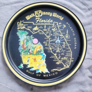 May include: A black and yellow round tray featuring a map of Florida with Walt Disney World landmarks. The tray has a yellow border and includes cartoon characters and the text "Walt Disney World Florida".