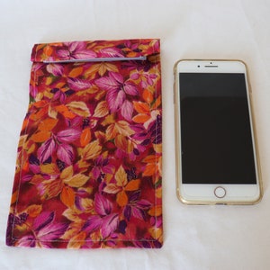 Op de afbeelding: Een rode, oranje en roze bloemenprint stoffen etui met een ritssluiting. Het etui ligt naast een witte smartphone met een zwart scherm.