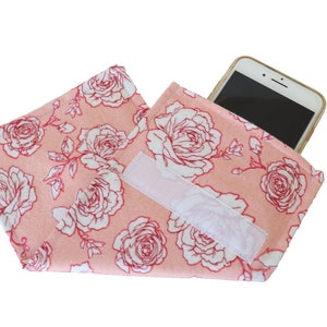 Op de afbeelding: Een roze stoffen tasje met een wit bloemenpatroon en een klittenbandsluiting. Een smartphone zit in het tasje.