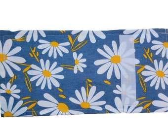 May include: A blue fabric pouch with a white velcro closure. The pouch is decorated with a white daisy pattern on a blue background. The daisies have yellow centers.