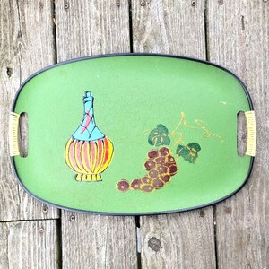 May include: A green serving tray with a black rim features a painted design of a bottle of wine and a bunch of grapes. The bottle is decorated with red, yellow, blue, and green stripes. The grapes are painted in shades of red, purple, and green.