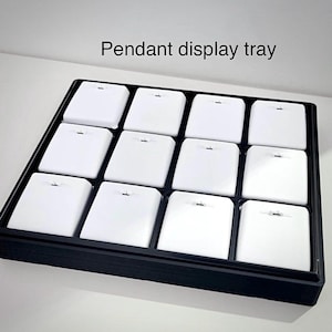 May include: Black display tray with 12 white square compartments for displaying pendants. The tray has the text "Pendant display tray" printed on the top.