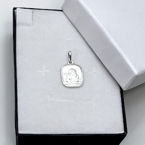 May include: A silver pendant featuring a detailed image of a cherub angel with wings. The pendant is in a white box with a black border.