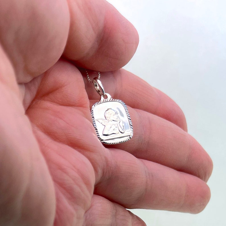 May include: Silver pendant necklace featuring a square charm with an embossed image of a praying angel.