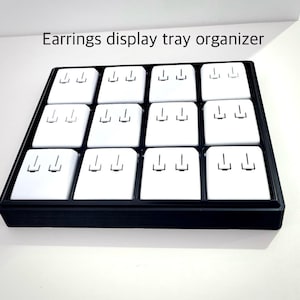 May include: Black earring display tray organizer with 12 individual compartments. Each compartment has three slots for holding earrings.