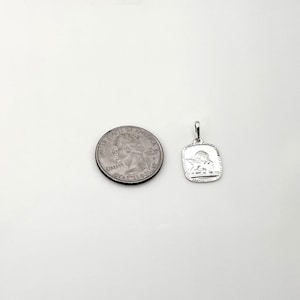 May include: Silver charm pendant featuring a detailed angel design. The pendant is approximately the size of a US quarter.