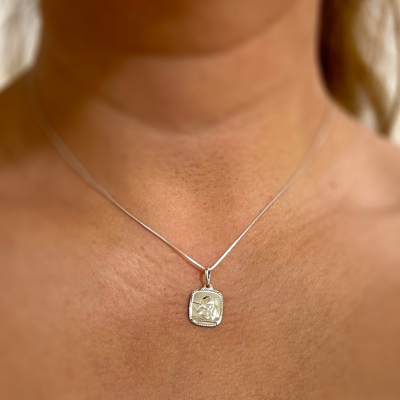 May include: A silver chain necklace with a small, square pendant featuring a detailed image of a person. The pendant has a slightly raised, textured border.