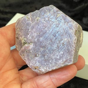 May include: A large, rough, purple and grey gemstone with a hexagonal shape. The gemstone has a natural, unpolished finish.