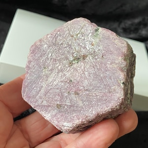 Puede incluir: Un gran cristal de rubí rosa en bruto con forma hexagonal. El cristal tiene una superficie natural sin pulir con estrías e inclusiones visibles.