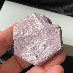 Puede incluir: Un gran cristal de rubí rosa facetado con una superficie rugosa y texturizada. El cristal tiene una forma hexagonal y un color rosa intenso.