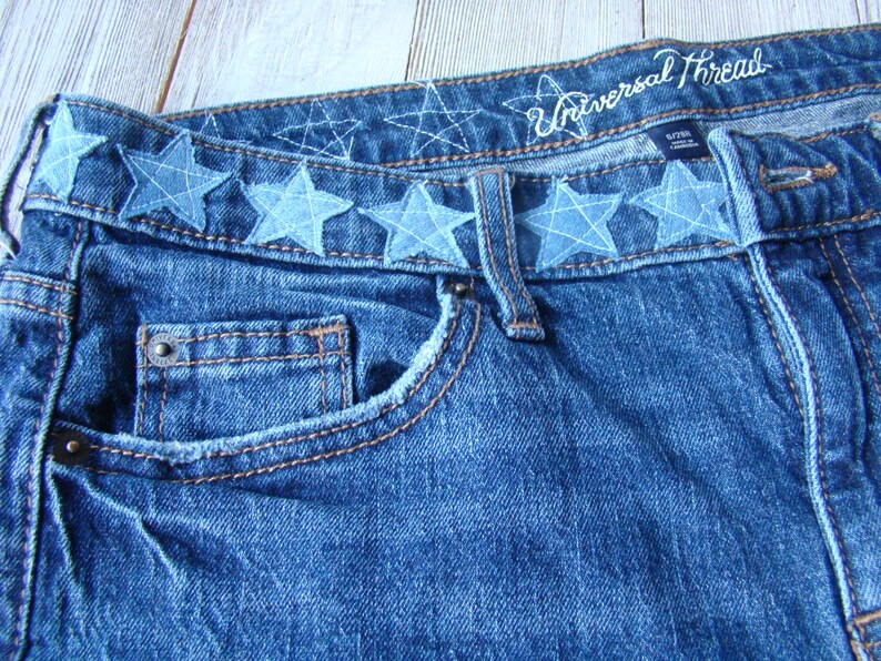 May include: Blue denim jeans with a waistband featuring a row of blue star-shaped embellishments. The waistband also has the text "Universal Thread" embroidered in white.