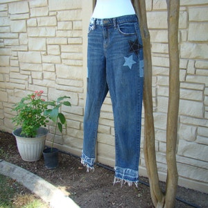 May include: Blue denim jeans with frayed hems and star-shaped patches. The patches are made of different fabrics and colors, including black, gray, and white.