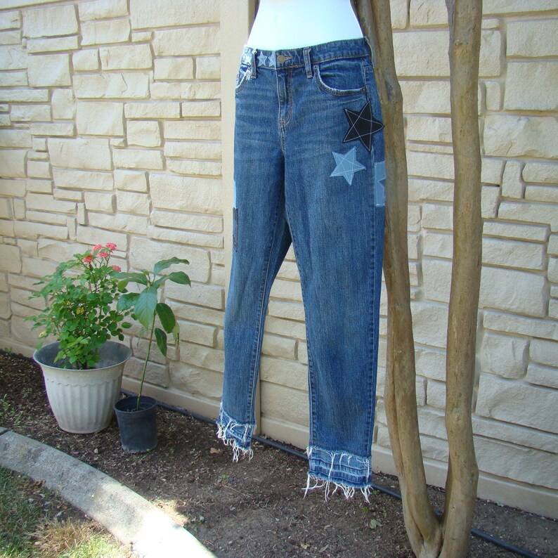 May include: Blue denim jeans with frayed hems and star-shaped patches. The patches are made of different fabrics and colors, including black, gray, and white.