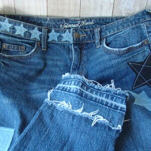 May include: Blue denim jeans with a frayed hem and a black star patch. The waistband has a row of embroidered stars and the text "Universal Thread".
