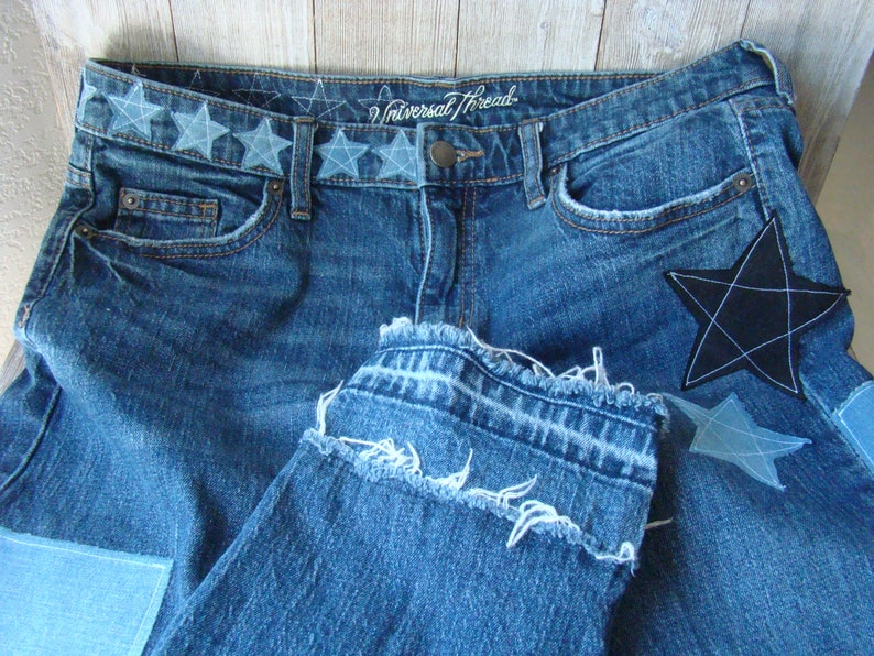 May include: Blue denim jeans with a frayed hem and a black star patch. The waistband has a row of embroidered stars and the text "Universal Thread".