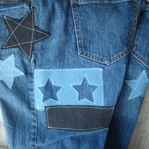 May include: Blue denim jeans with multiple star-shaped patches sewn on. The patches are in various shades of blue and black.