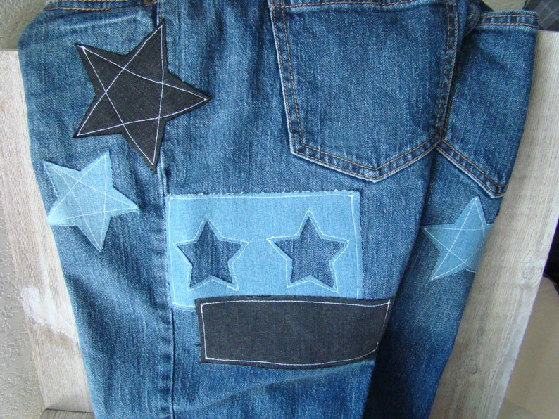 May include: Blue denim jeans with multiple star-shaped patches sewn on. The patches are in various shades of blue and black.