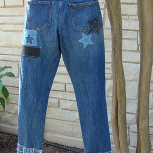 May include: Blue denim jeans with frayed hems and star-shaped patches. The patches are in shades of blue and black.