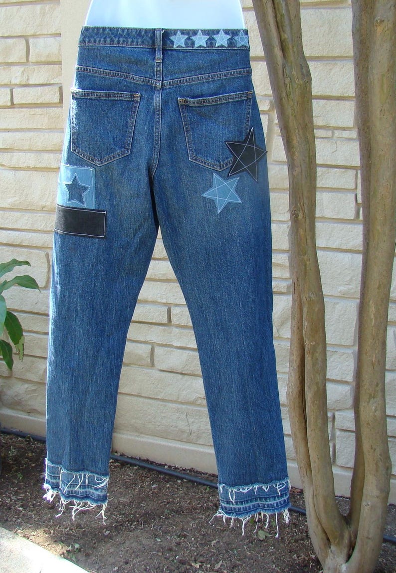 May include: Blue denim jeans with frayed hems and star-shaped patches. The patches are in shades of blue and black.