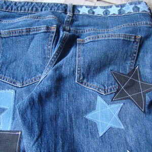May include: Blue denim jeans with a row of blue stars across the waistband and several star-shaped patches sewn on the back pockets. The patches are in various shades of blue and black.