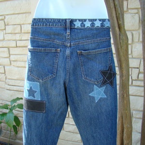 May include: Blue denim jeans with a black and blue star patch on the back pocket and a row of blue stars across the waistband.