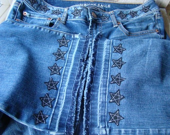 May include: Blue denim jeans with a frayed hem and black star-shaped embroidery along the seams. The waistband has the text "American Eagle" in white.