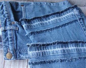 May include: A pair of blue denim jeans with frayed edges along the seams. The jeans have a button fly and a single button on the waistband.