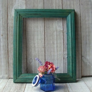 May include: A blue glass jar with a white lid and dried flowers inside, sitting in front of a green wooden picture frame.