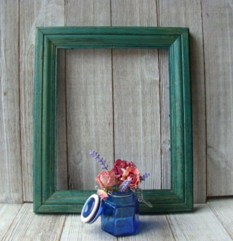 May include: A blue glass jar with a white lid and dried flowers inside, sitting in front of a green wooden picture frame.