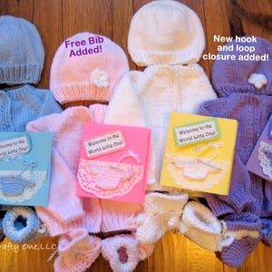 May include: Hand-knitted baby clothing sets in blue, pink, white, and purple. Each set includes a hat, sweater, booties, and a greeting card that says "Welcome to the World Little One!". The image also includes the text "Free Bib Added!" and "New hook and loop closure added!"