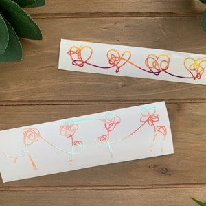Pode incluir: Dois adesivos de vinil holográficos com um design de arte de linha. O primeiro adesivo apresenta três corações conectados em um degradê de laranja, amarelo e vermelho. O segundo adesivo apresenta quatro flores conectadas em um degradê de rosa, laranja e azul.
